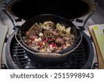 outdoor cooking - goulash from venison meat with wild berries, onions, herbs and apple in a dutch oven on a charcoal grill at a autumn day