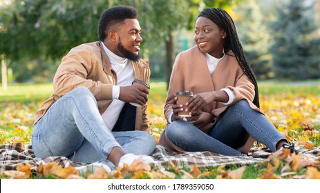 Outdoor Date Ideas Concept. Smiling African American Couple Drinking Takeout Coffee While Sitting On Picnic In Autumn Park