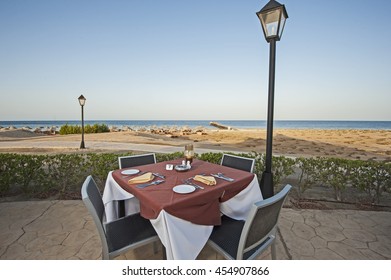 Outdoor Dining Area With Table Set Up On Tropical Ocean Beach Of Luxury Hotel Resort