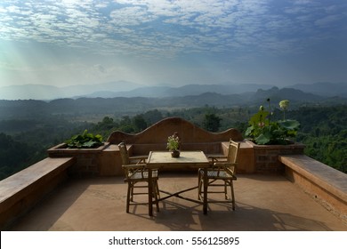 Outdoor dining on the roof of resort building in southeast Asia overlooking lush green hills of padi fields and farms sun rays beaming through clouds