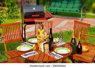 Outdoor Dining Or Picnic Scene In Backyard. BBQ Grill In Background. Tilt-shift Effect.