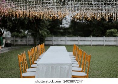 Outdoor dining setup with white table cloth under the fairy light on the green field