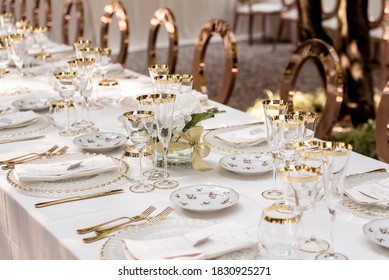Outdoor dining table dressed elegantly with white linen tablecloth, crystal platters, floral china, gold-plated cutlery and gold-trimmed glasses