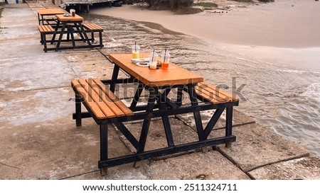 Outdoor dining table set on the beach with drinks and snacks. Relaxed atmosphere at a beachside cafe with sea view. Evening view at a beachside cafe with wooden tables and chairs.