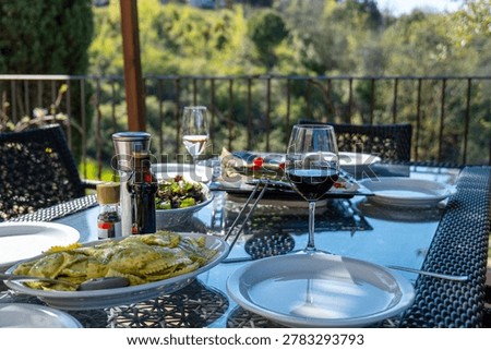 Outdoor dining table set with wine glasses, plates, and fresh food on a terrace overlooking the Tuscan landscape. A relaxed meal in a scenic countryside setting.