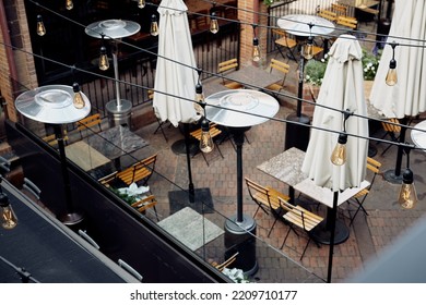 Outdoor Dining Tables At A Restaurant With String Lights Hanging Above Located In A Shopping Plaza.  