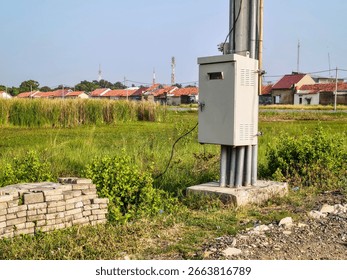 Outdoor electrical control panel mounted on utility pole near brick house with tiled roof, used for power distribution and street lighting management.
