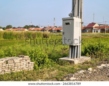 Outdoor electrical control panel mounted on utility pole near brick house with tiled roof, used for power distribution and street lighting management.
