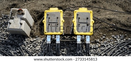 Outdoor electrical junction boxes with multiple cables laid on gravel ground, showing temporary power distribution, industrial setup, and construction site infrastructure.
