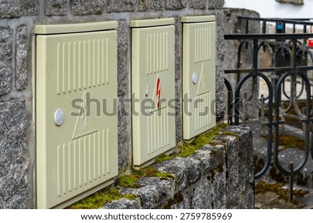 Outdoor electrical meter boxes mounted on a stone wall, beige power distribution cabinets with high voltage warning signs, technical infrastructure and utility enclosures on a granite facade near rail