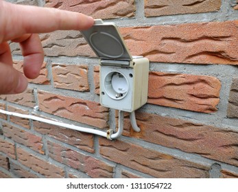 Outdoor Electrical Socket With Child Protection And The Cover Lifted By Man's Finger Is Mounted On The Brick Wall 