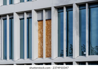 Outdoor exterior front view of modern facade with typical rectangular modern narrow vertical windows and one part of broken window which closed by OSB board.