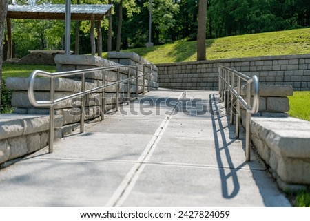 Outdoor, exterior gray concrete ramped sidewalk with stainless steel railings. 