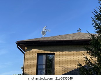 Outdoor external satellite antenna and directional TV antenna, on the roof of a brick cottage house with a window. General view of the house against the blue sky. satellite TV installation 