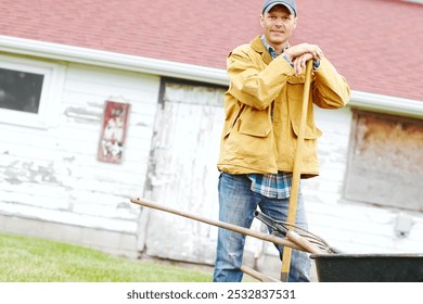 Outdoor, farm and man in portrait with wheelbarrow, gardening and agriculture with confidence by shed. Countryside, male person and farmer with equipment for transport, cleaning and spade as tools - Powered by Shutterstock