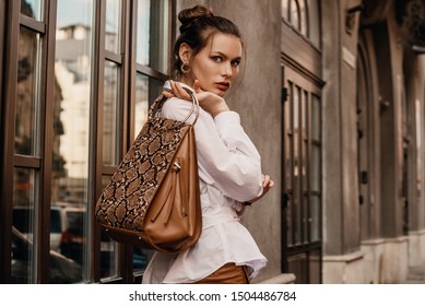 Outdoor Fashion Portrait Of Elegant, Luxury Woman Wearing Trendy White Shirt, Holding Stylish Beige, Brown Reptile, Snakeskin, Python Print Bag, Handbag, Posing In Street. Copy, Empty Space For Text 