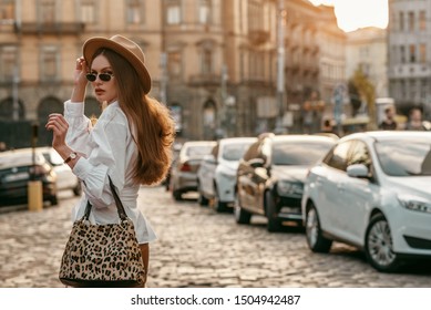 Outdoor Fashion Portrait Of Elegant, Luxury Woman Wearing Beige Hat, Sunglasses, Trendy White Shirt, Brown Wrist Watch, Holding Animal, Leopard Print Bag, Walking In Street. Copy, Empty Space For Text