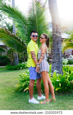 Outdoor fashion portrait of handsome stylish man and his pretty young girlfriend posing at hot summer day at neon stylish casual outfits and sunglasses, holding hands and hugs.