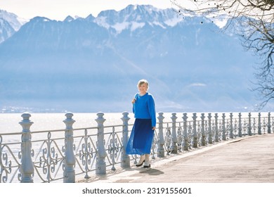 Outdoor fashion portrait of happy mature woman walking by the lake, wearing blue  pullover and skirt