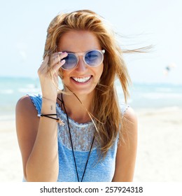 Outdoor fashion portrait summer beach style of young beautiful blonde woman fresh face smiling on the beach of tropic island having fun on vacation in blue dress and sunglasses 