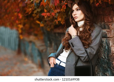 Outdoor fashion portrait of young beautiful fashionable woman wearing white turtleneck, grey checked blazer, wrist watch, holding small leather bag, posing in autumn street. Copy, empty space for text