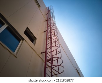Outdoor fire escape ladder on industrial building wall. Bottom up view. Fire escape on building facade. Roof access ladder