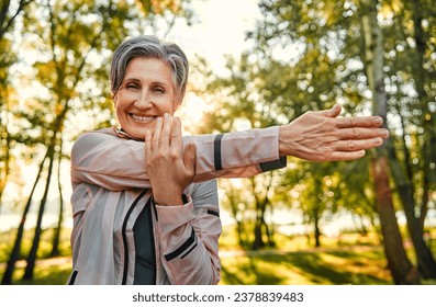 Outdoor fitness during retirement. Portrait of aged lady with stylish haircut doing physical activity in park. Lively female dressed in sportswear making cardio exercises and stretching arms. - Powered by Shutterstock