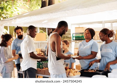 Outdoor food distribution event orchestrated by non-profit, attracting individuals of all races, willing to contribute to welfare of underprivileged. Volunteers supporting the needy with warm meals.
