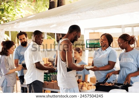Outdoor food distribution event orchestrated by non-profit, attracting individuals of all races, willing to contribute to welfare of underprivileged. Volunteers supporting the needy with warm meals.