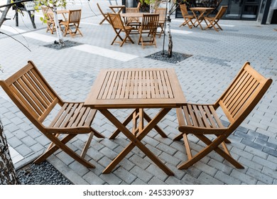 Outdoor furniture set including a wooden table and chairs, placed on a brick sidewalk. The furniture is made of natural material with a wood stain finish - Powered by Shutterstock