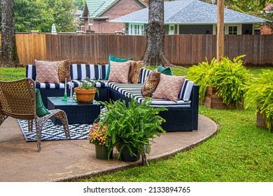 Outdoor furniture - striped sectional on round patio with area rug and chair and ferns with trees and neighboring houses in background - Shutterstock ID 2133894765