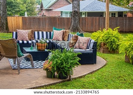 Outdoor furniture - striped sectional on round patio with area rug and chair and ferns with trees and neighboring houses in background