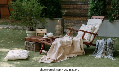 Outdoor garden wooden furniture at autumn nature, green grass. Nobody at home backyard with chair, lounge. Relax at outside terrace with blankets, pillows at retro, vintage decoration.