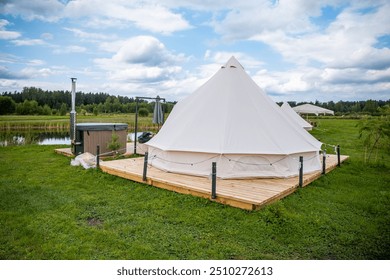 Outdoor glamping setup with a wooden deck, hot tub, and tent on a grassy field under a cloudy sky. - Powered by Shutterstock