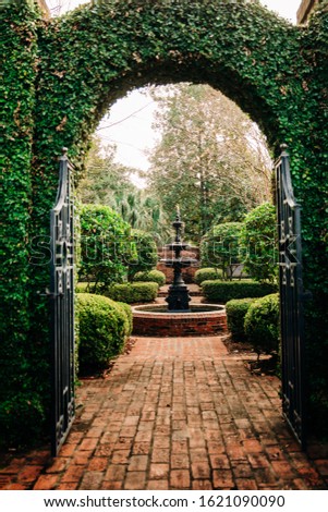 Outdoor Green secret garden with arched entry and gate and a fountain in the middle and red brick and black iron gate