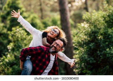 Outdoor Happy And Cheerful Caucasian Couple With Glasses Have Fun And Enjoy The Nature And Leisure Activity Together - Man Carry Woman And Both Laugh A Lot