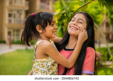 Outdoor Image Of Happy, Cheerful Little Girl Pulling The Cheeks Of Her Aunt. They Are Having Fun Together In The Fresh Air.