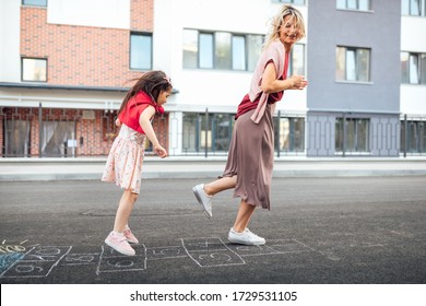 Outdoor Image Of Happy Little Girl Playing Hopscotch With Her Mother On Playground Outdoors. Child Plays With Her Mom Oustside. Kid Plays Hopscotch Drawn On Pavement. Activities And Games For Children