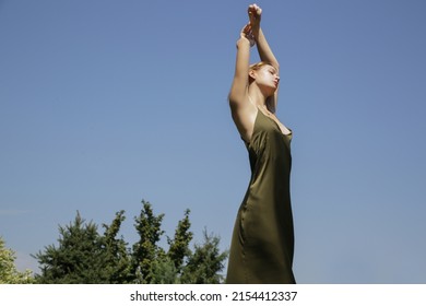 Outdoor image of young woman in long green silk dress  against clear blue sky	