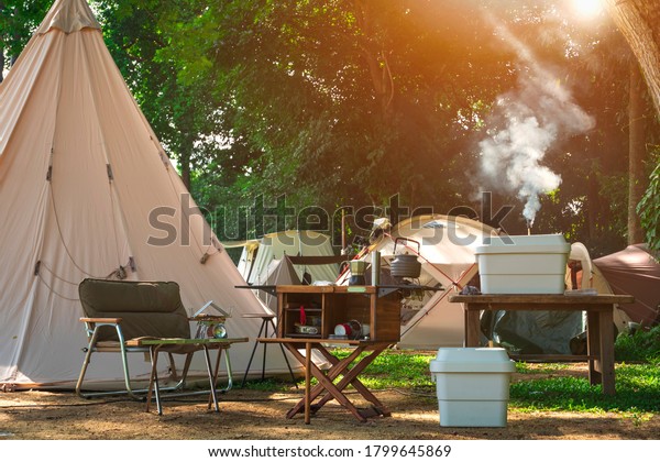 Outdoor kitchen\
equipment and wooden table set with field tents group in camping\
area at natural\
parkland