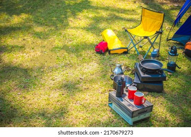 Outdoor Kitchen Equipment And Yellow Chair, Lantern, Mug  In Camping Area. Set Of Camping Equipment