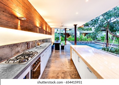 Outdoor kitchen with a stove an countertop next to garden including a pool in luxury hotel or house