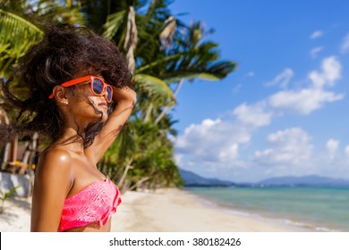 Outdoor Lifestyle Close-up Of Black Beautiful Teenage Girl In Pink Bra And Sunglasses. Young Hipster Woman Play With Her Hair. She Is Happy. Sunny Hot Summer Day At Tropical Sea Beach With Palms.