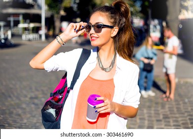 Outdoor lifestyle funny and sunny portrait of young stylish hipster girl walking on street,smiling and laughing on the city,wearing cute trendy outfit,drinking hot latte,travel with backpack,coffee
