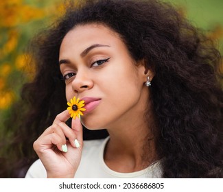 Outdoor Lifestyle Portrait Of African American Young Woman With Flower. Dark-skinned Brunette Female With Loose Wavy Curls. Hipster Mixed Race Black African Girl. Soft Focus.