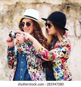 Outdoor lifestyle portrait of two best friends hipsters making photo on their vintage camera, having fun together, joy and happiness, wearing trendy bright clothes and sunglasses.