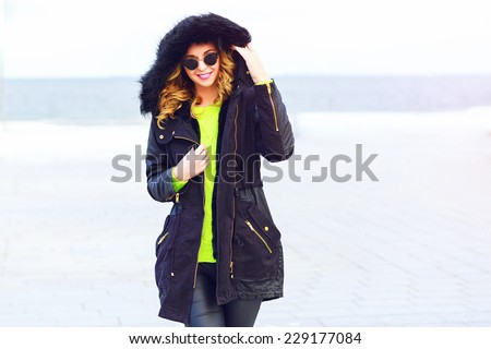 Outdoor lifestyle wither portrait of stylish young woman wearing neon swather and casual black parka jacket. Street style look.