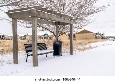 Outdoor Metal Bench Under A Wooden Pergola Against Snowy Terrain In Winter