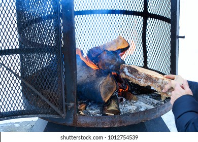 Outdoor Metallic Fireplace In Winter Season Charged With Firewood, In The Burning Process. Wood-burning Fire Pit With Removable Fire Pan And With Wide Bar Ribs And Handles. Winter Outdoor Activity.