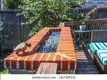 Outdoor Natural Gas Fire Pit With Low Flames On Patio With Privacy Fence In Background And Colorful Seating